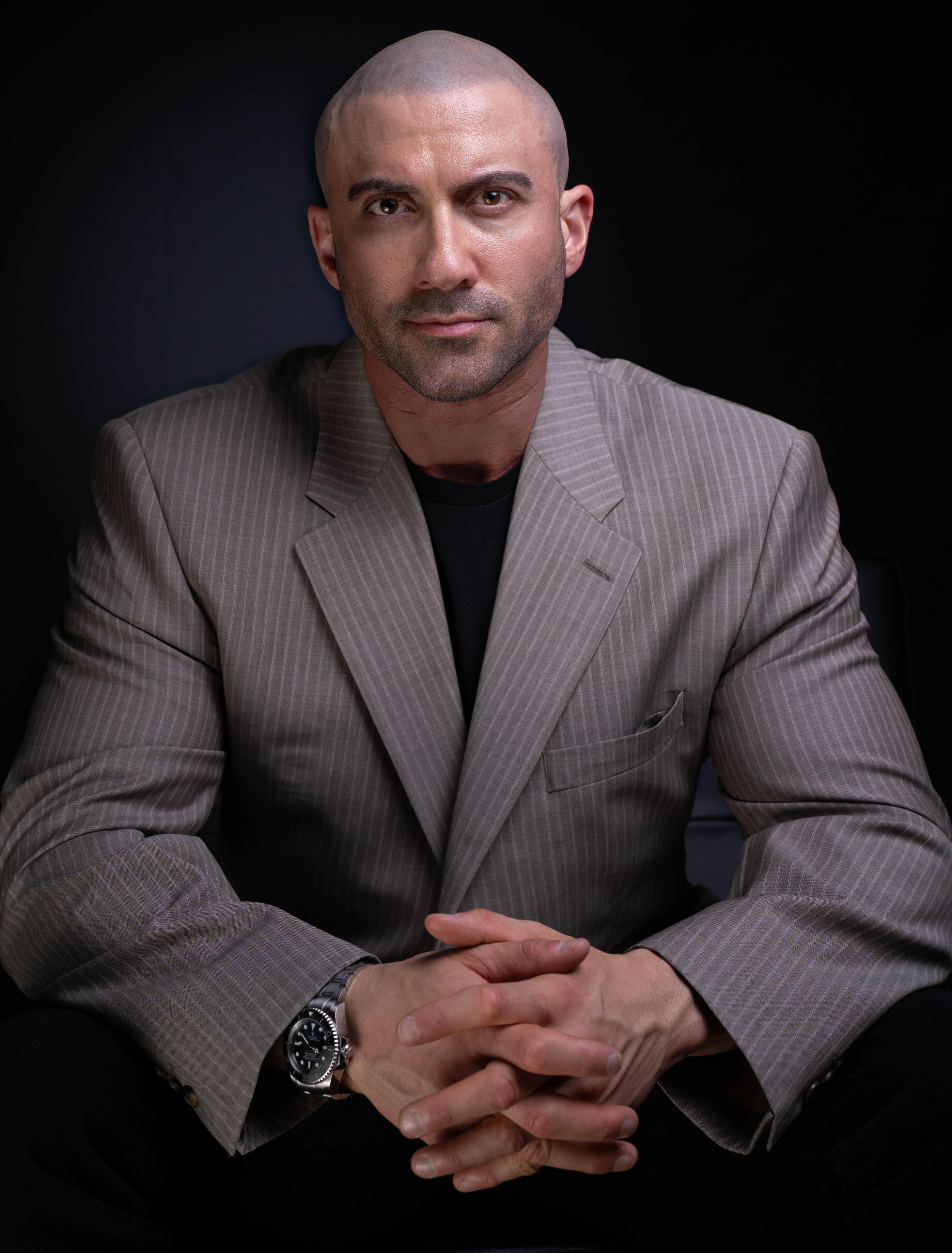 Author Thomas Rooney (Tom Rooney), sitting in a black Barcelona chair wearing long brown leather blazer, promoting Reflections of a Male Revue Headliner: How to Win at Life and Love